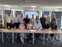 Picture of VCFSE and Public Sector leaders around a long table with two individuals signing the MoU document