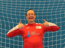 Photo of man smiling into the camera with a thumbs up gesture wearing a red shirt. Background includes a goalkeepers football net.