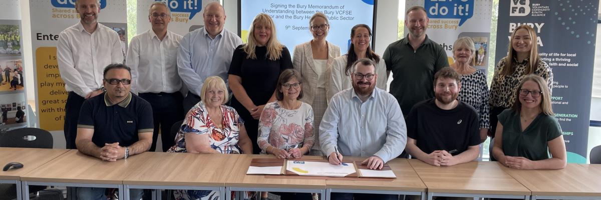 Picture of VCFSE and Public Sector leaders around a long table with two individuals signing the MoU document