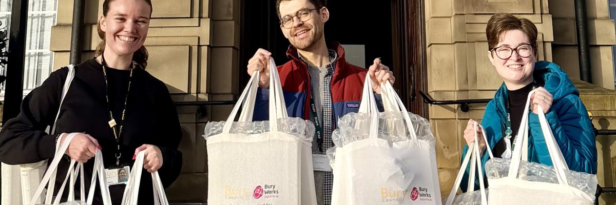 photograph of three people holding up bags smiling into the camera, with a historic building in the background