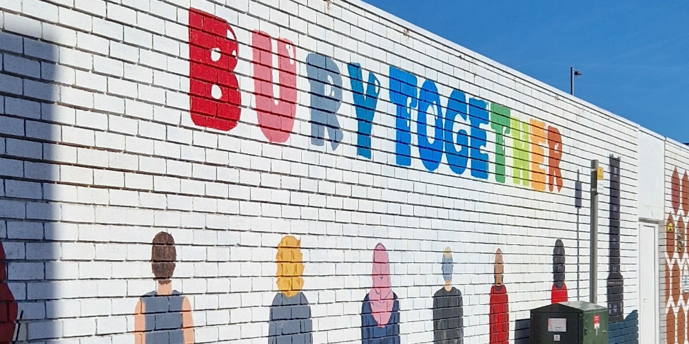A picture of a painted brick wall with people and the phrase Bury Together