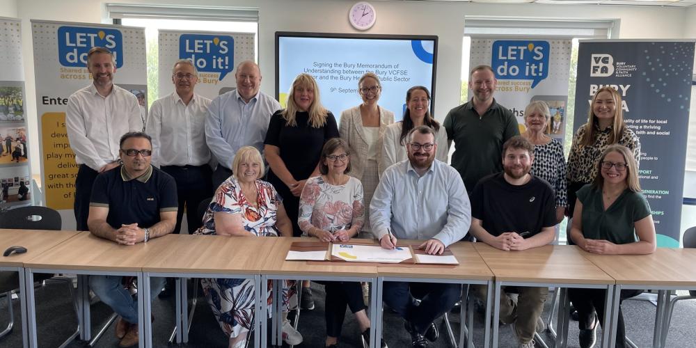 Picture of VCFSE and Public Sector leaders around a long table with two individuals signing the MoU document