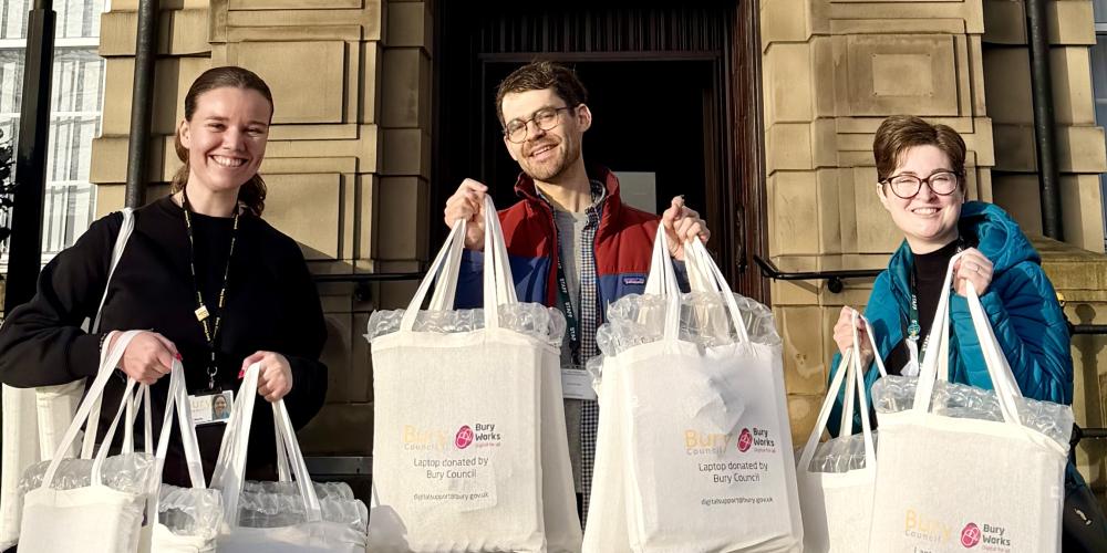photograph of three people holding up bags smiling into the camera, with a historic building in the background