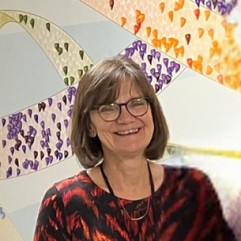 Picture of Jill - a lady wearing glasses, short bobbed hair and a red and black top smiling